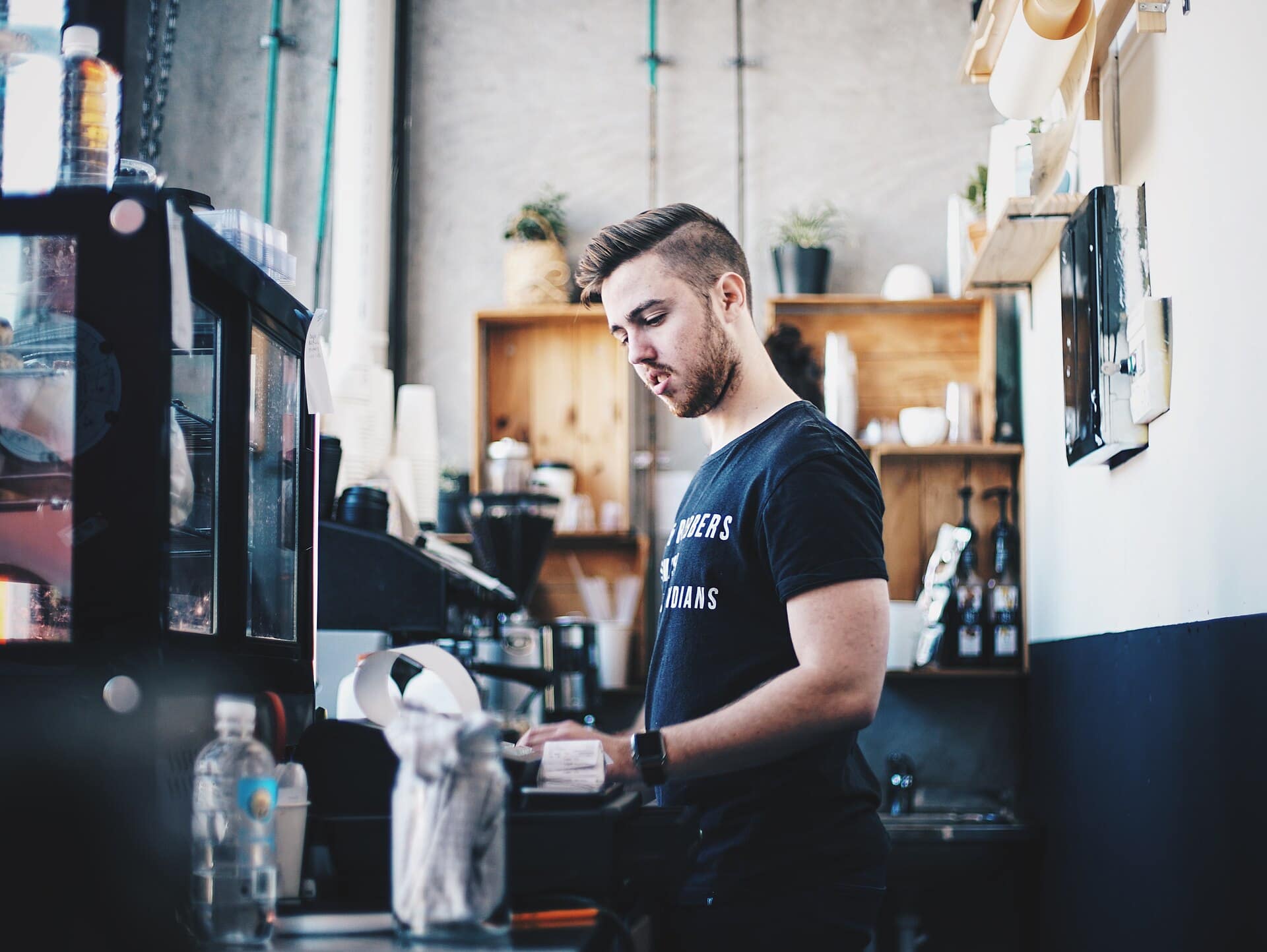 A café owner behind his counter, checking his phone.