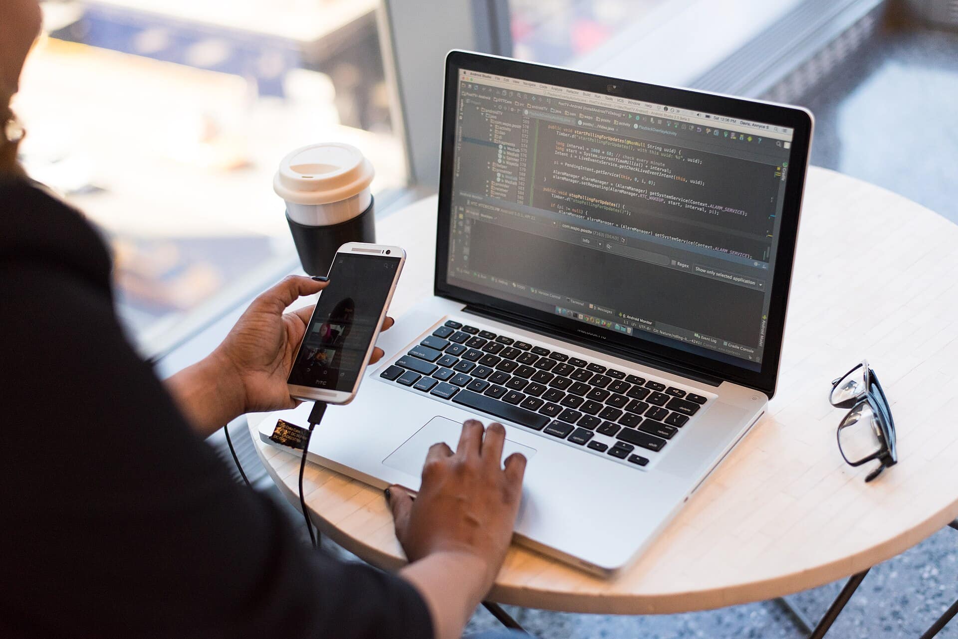 Hands typing on a laptop showing code, next to a coffee and a phone.