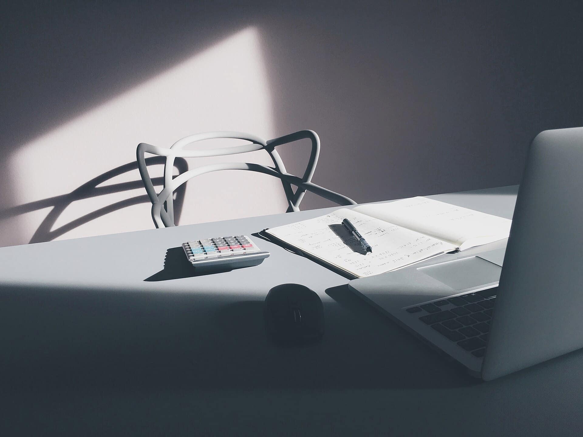 A desk with a laptop, an open notebook and a calculator.